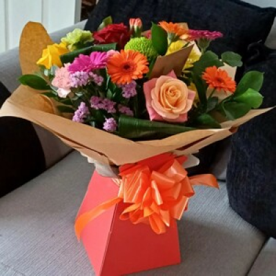 Celebration orange fizz. - Pop of blooms of the day, roses. Geberas, shamrock. Chrysanthemum. Mixed Foliage.